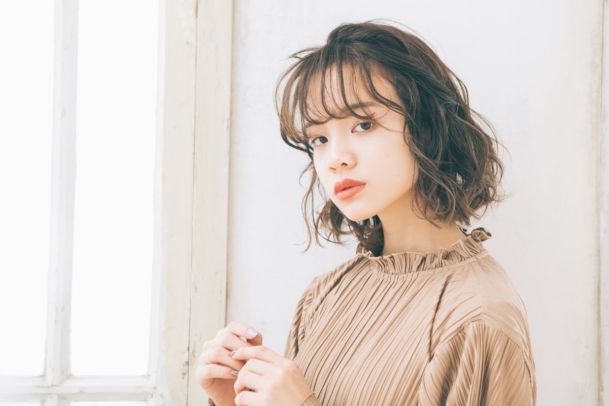 Cô gái mặc áo có cổ màu nâu be với kiểu tóc xoăn chữ S ngắn