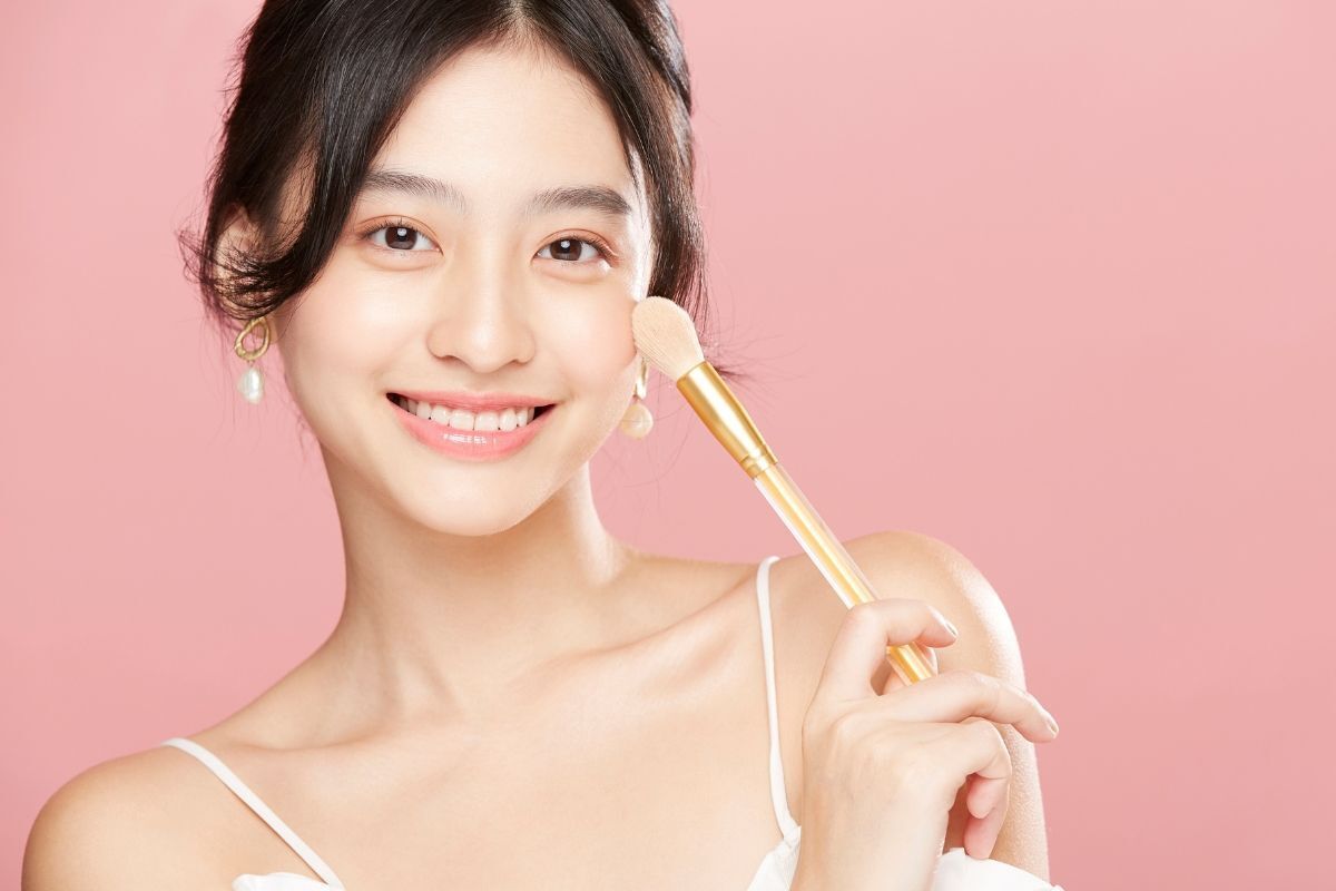 Cô gái cầm cây cọ màu be trang điểm tông màu mắt hồng nhạt