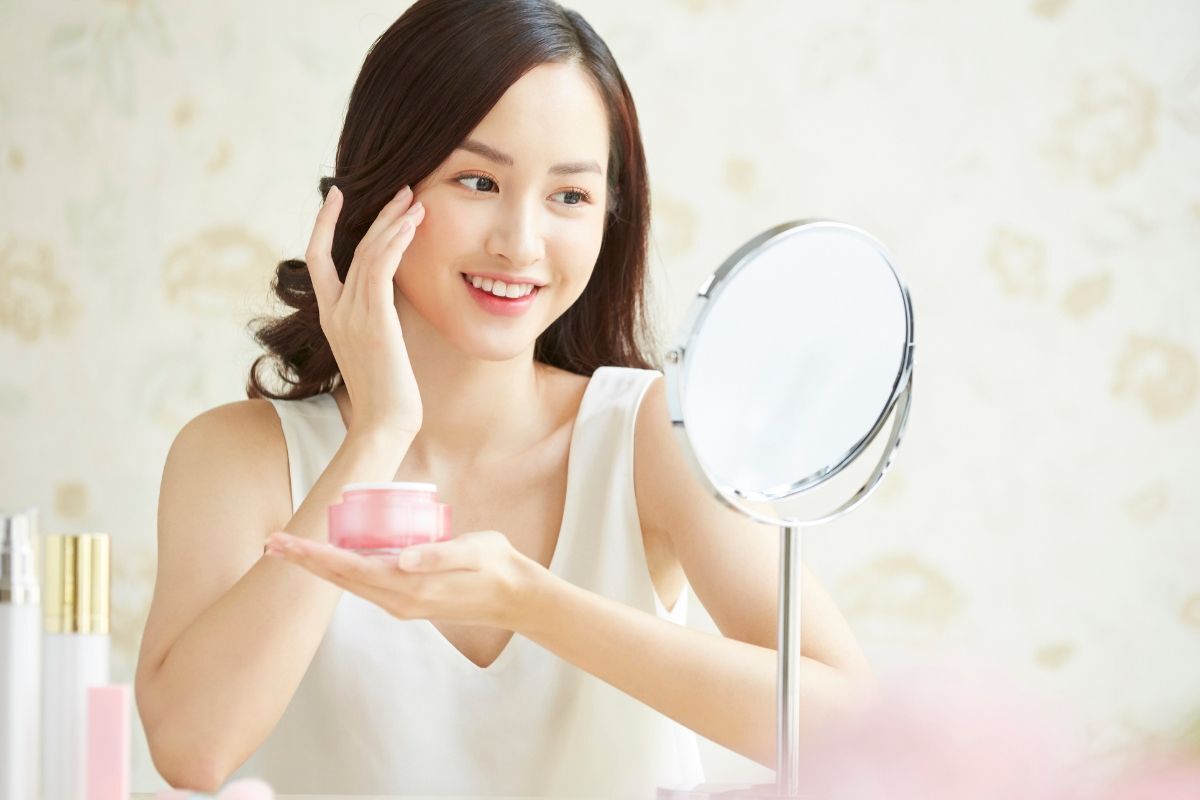 Cô gái có mái tóc xoăn dài sử dụng kem dưỡng ẩm để trị nẻ mặt