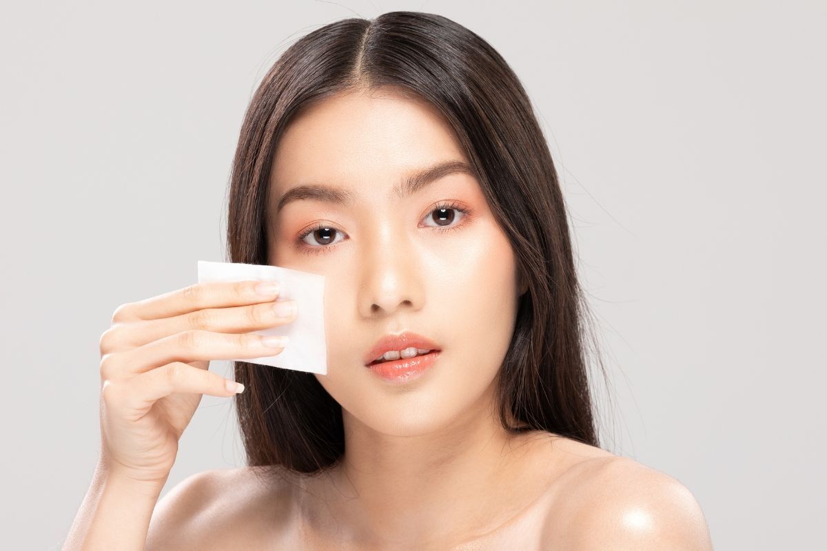 Cô gái có mái tóc rẽ ngôi giữa đang cầm miếng bông tẩy trang 