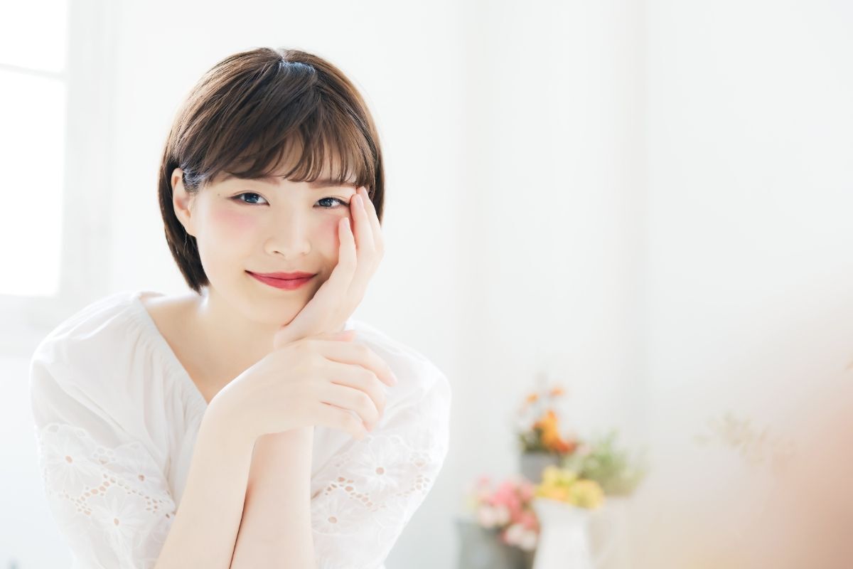 kiểu tóc cho gương mặt tròn cô gái mặc áo trắng mái thưa tóc tém ngắn sát cổ tay để lên má mỉm cười 