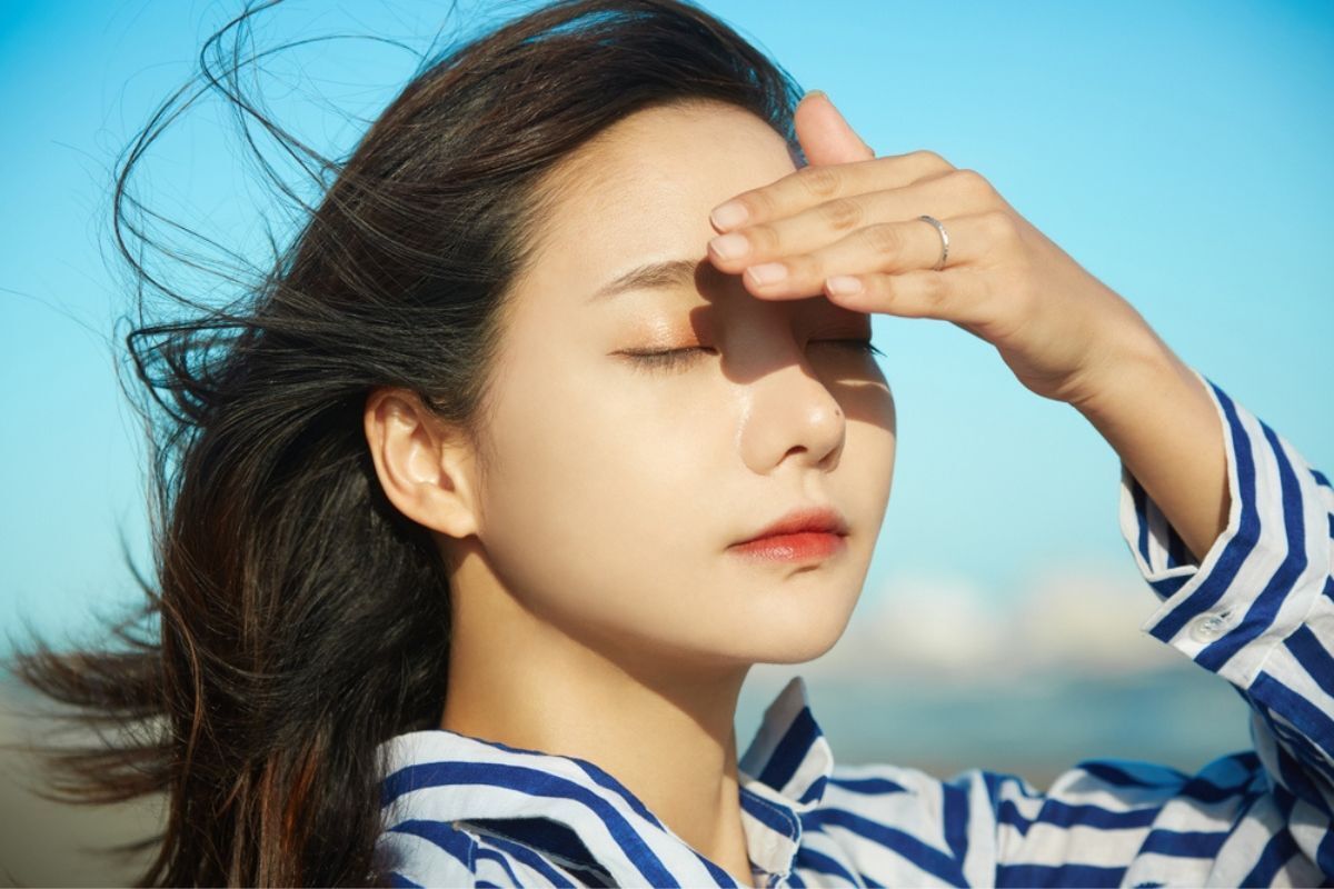 da sần sùi đừng quên thoa kem chống nắng cô gái mặc áo sơ mi kẻ sọc xanh đang nhắm mắt lại và một tay che nắng