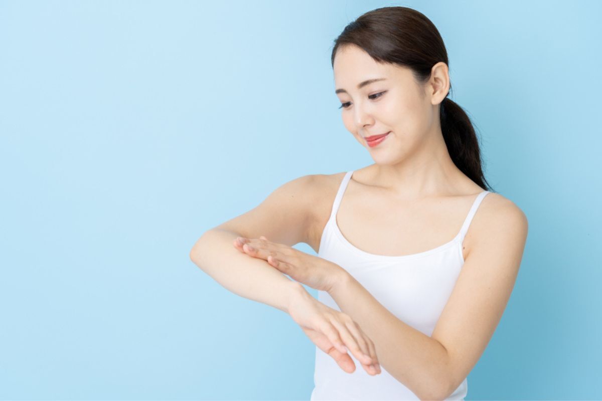da sần sùi cách trị da body sần sùi và xỉn màu cô gái mặc áo hai dây màu trắng đang chạm vào cánh tay phía sau nền màu xanh dương