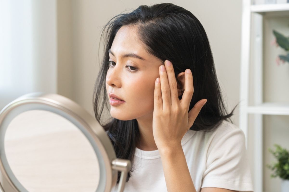 hyaluronic acid chống lão hóa cô gái nhìn vào gương lấy các ngón tay đẩy da mặt lên