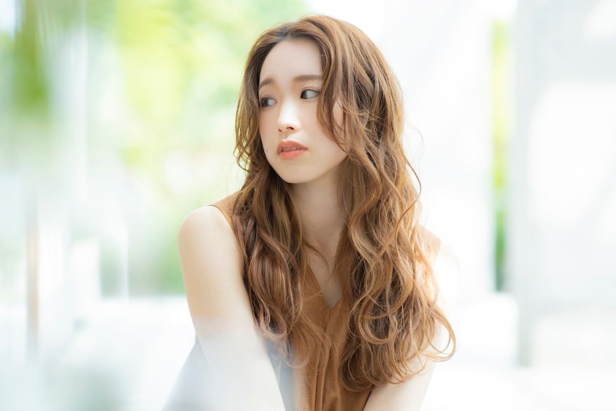 Chọn màu nhuộm tóc phù hợp với làn da cô gái có mái tóc xoăn sóng nước màu nâu vàng đang nhìn sang trái