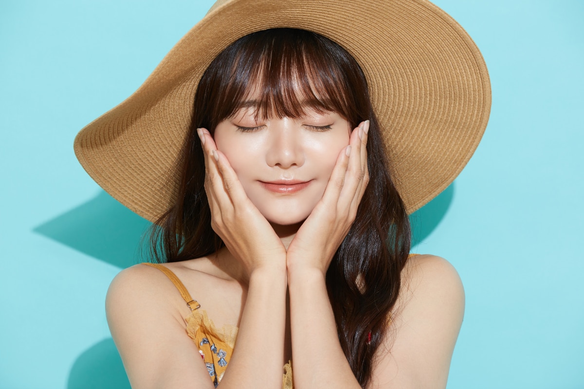 skincare cho da dầu mụn cô gái đội mũ rộng vành và thoa kem chống nắng cho da dầu mụn