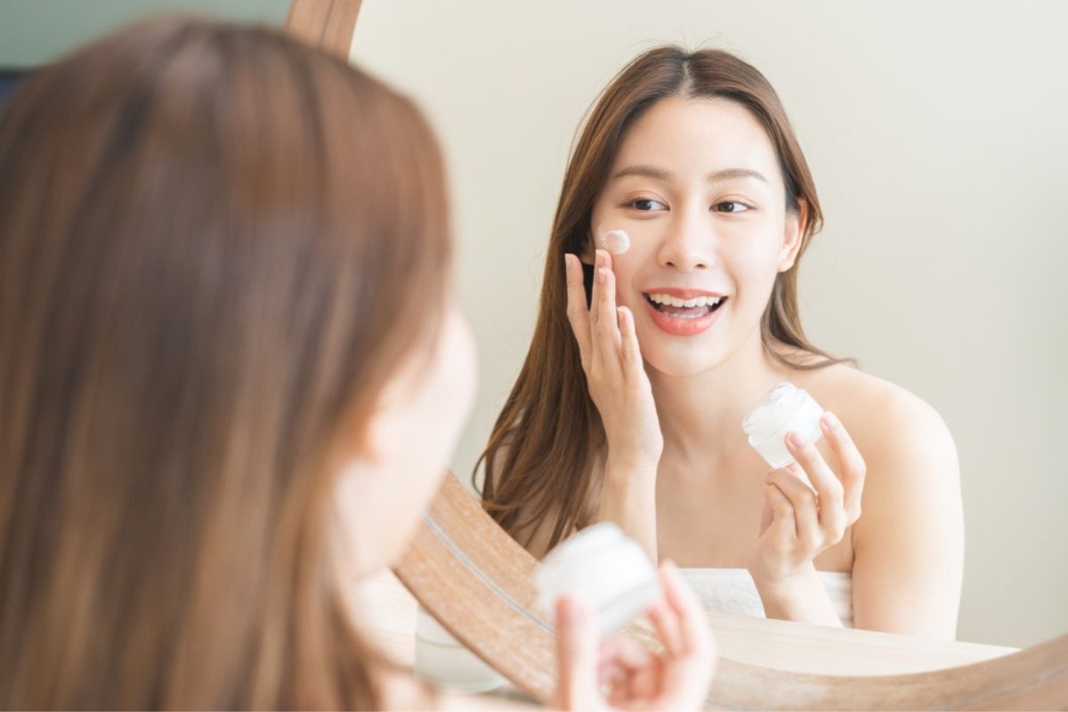 chườm đá lên mặt tiếp tục các bước skincare còn lại cô gái soi gương thoa kem dưỡng lên mặt