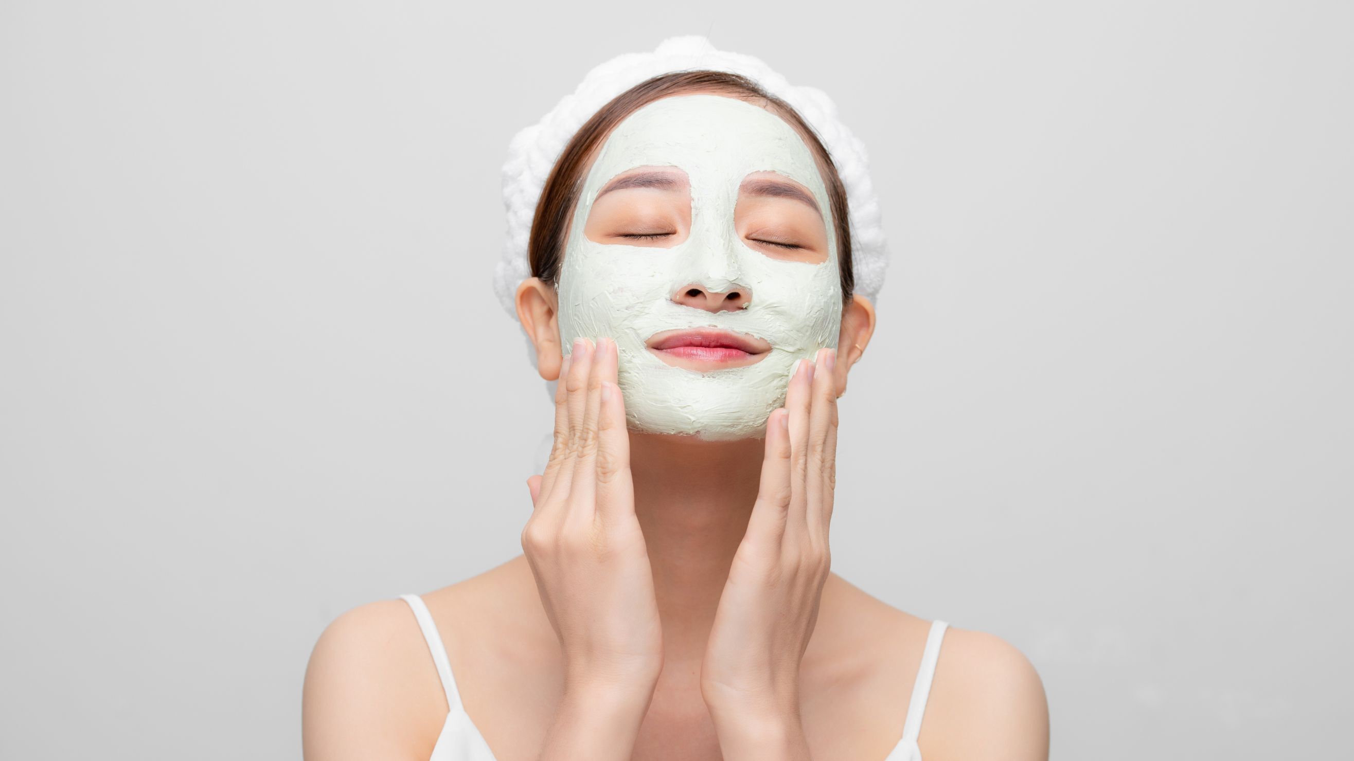 Cô gái nhắm mắt với hai bàn tay chạm lên má, đắp mặt nạ màu xanh lá nhạt