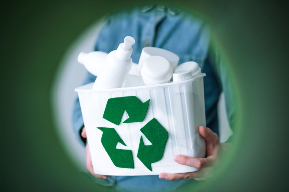 bao bì mỹ phẩm từ nhựa tái chế sau tiêu dùng tay người phụ nữ cầm hộp màu trắng đựng vỏ chai nhựa vứt vào thùng rác màu xanh lá cây