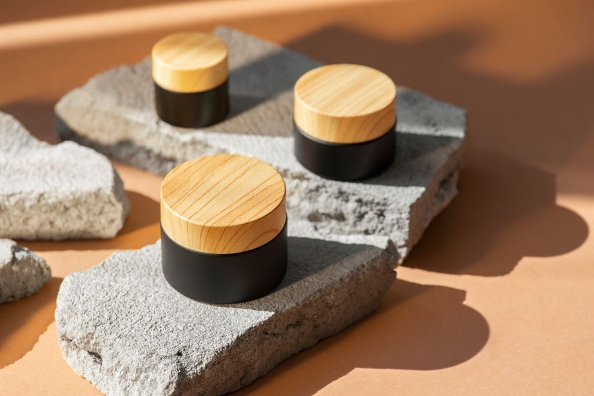 bao bì mỹ phẩm từ tre hũ mỹ phẩm nắp gỗ màu đen chứa lotion đặt trên bục bê tông xám để trưng bày