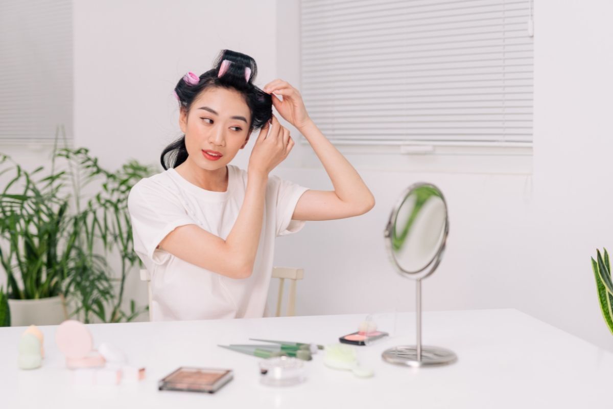 cách uốn tóc tại nhà cô gái ngồi trước gương nhỏ xài lô uốn tóc mặc áo thun trắng