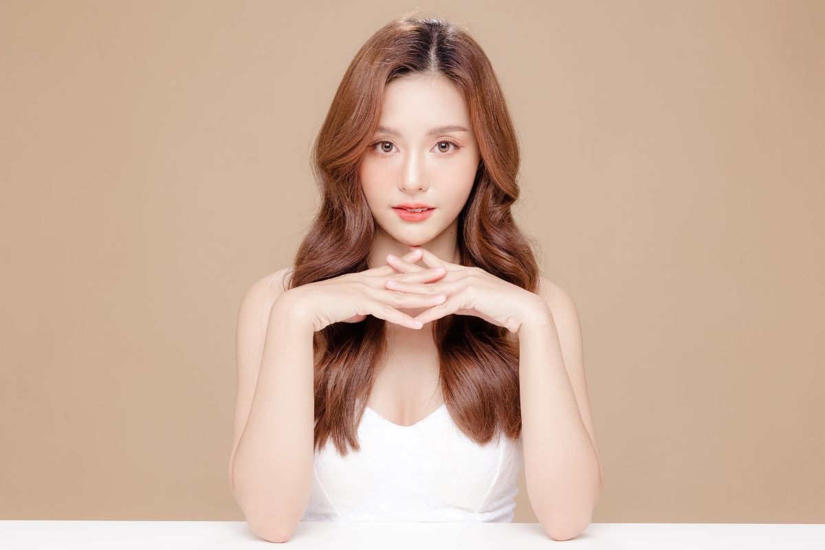 Những kiểu tóc nhuộm màu vàng đồng đẹp nhất cô gái mặc áo trắng hai tay đan vào nhau trên nền nâu be