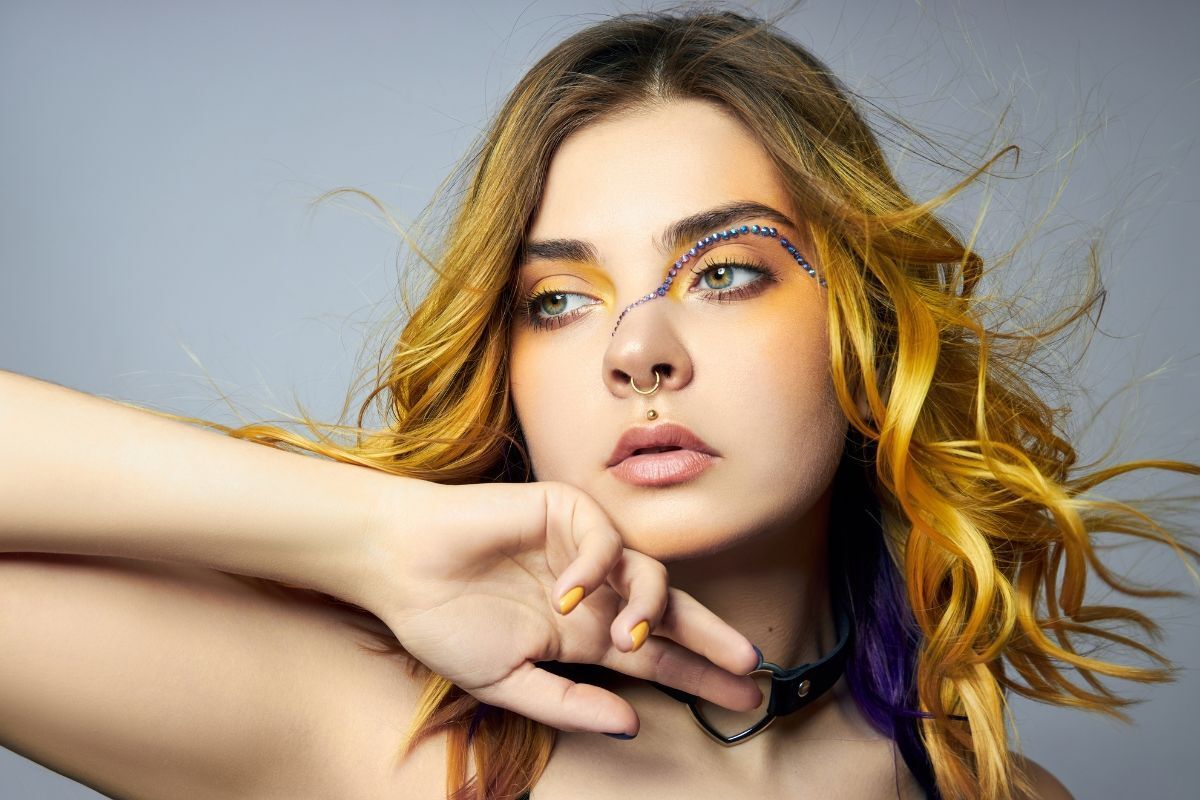 tóc màu vàng chanh cô gái đưa một tay chạm vào cằm và tóc bay trong gió trên nền màu xám