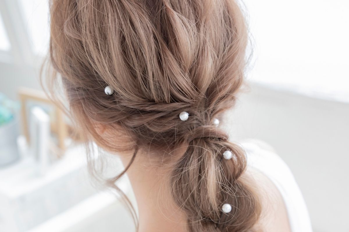 tóc màu nâu tây ánh khói cô gái thắt bím đính ngọc trai lên tóc ngồi quay lưng mặc đầm trắng