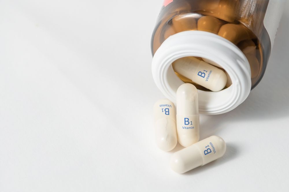 vitamin b1 có tác dụng gì cho tóc hủ thuốc thuỷ tinh màu cam đang đổ các viên thuốc con nhộng màu trắng ra mặt bàn màu trắng