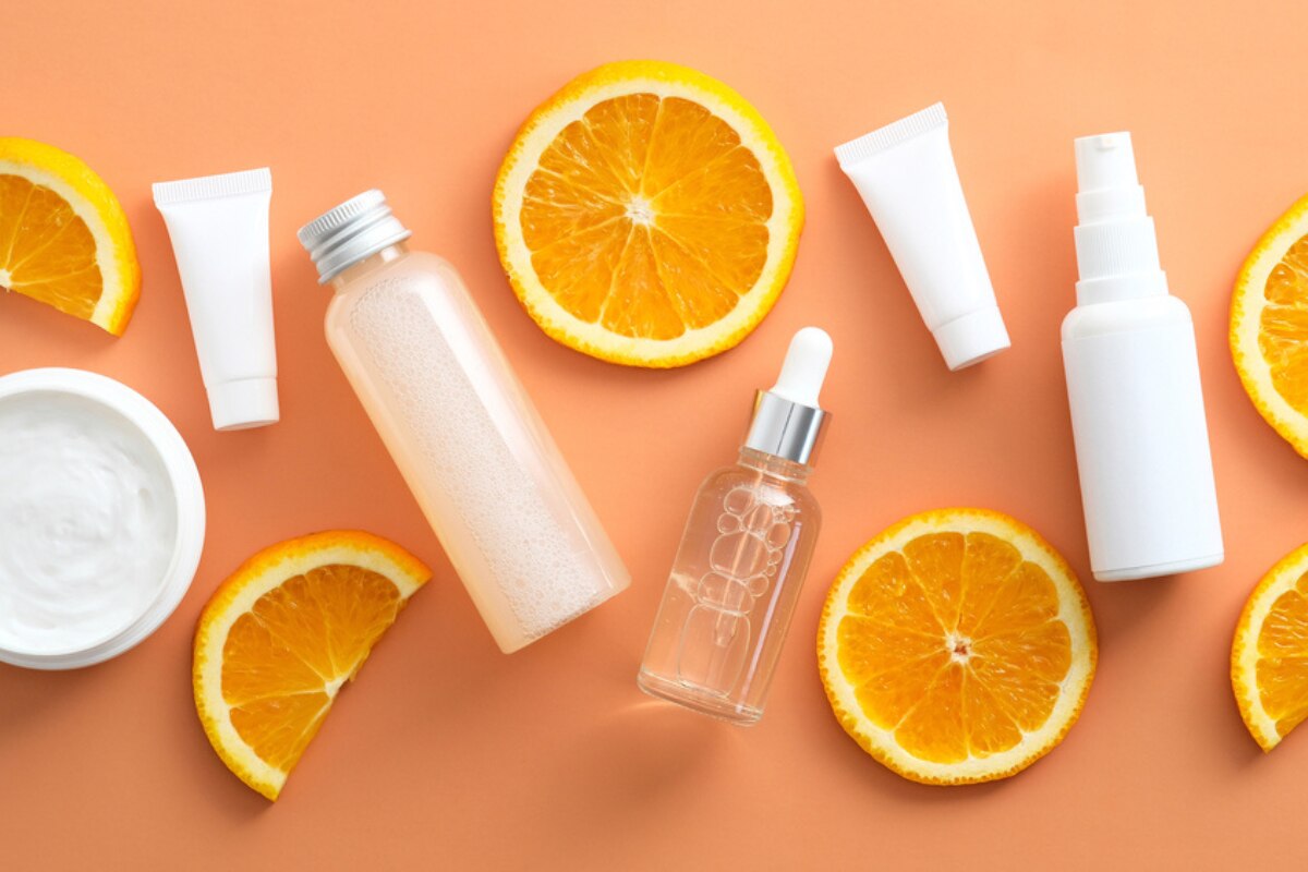  vitamin c có tác dụng gì với da mặt chai lọ hũ màu trắng nằm xen kẽ các lát cam trên nền cam