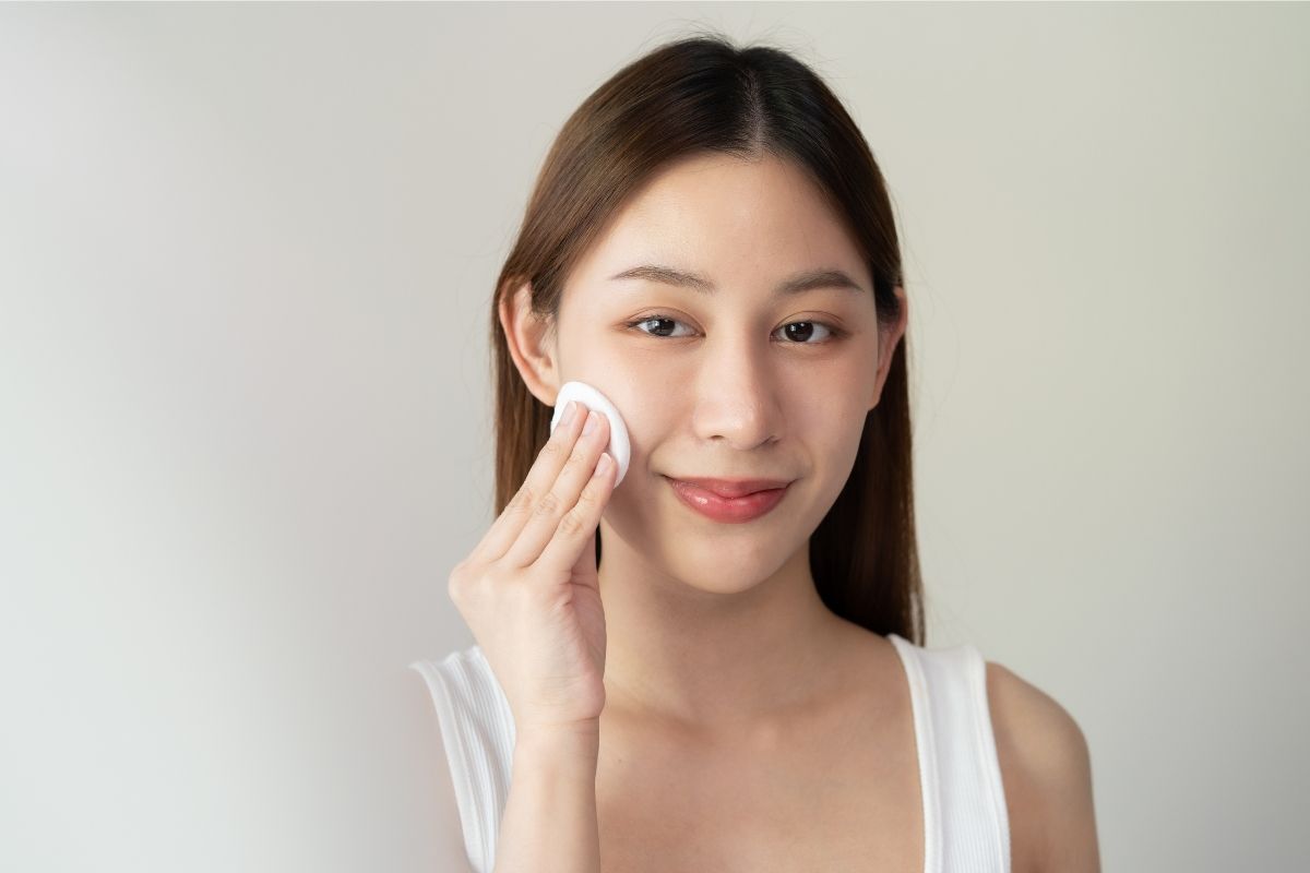 Toner pad công dụng của toner pad cô gái đang thoa miếng bông tròn màu trắng lên má