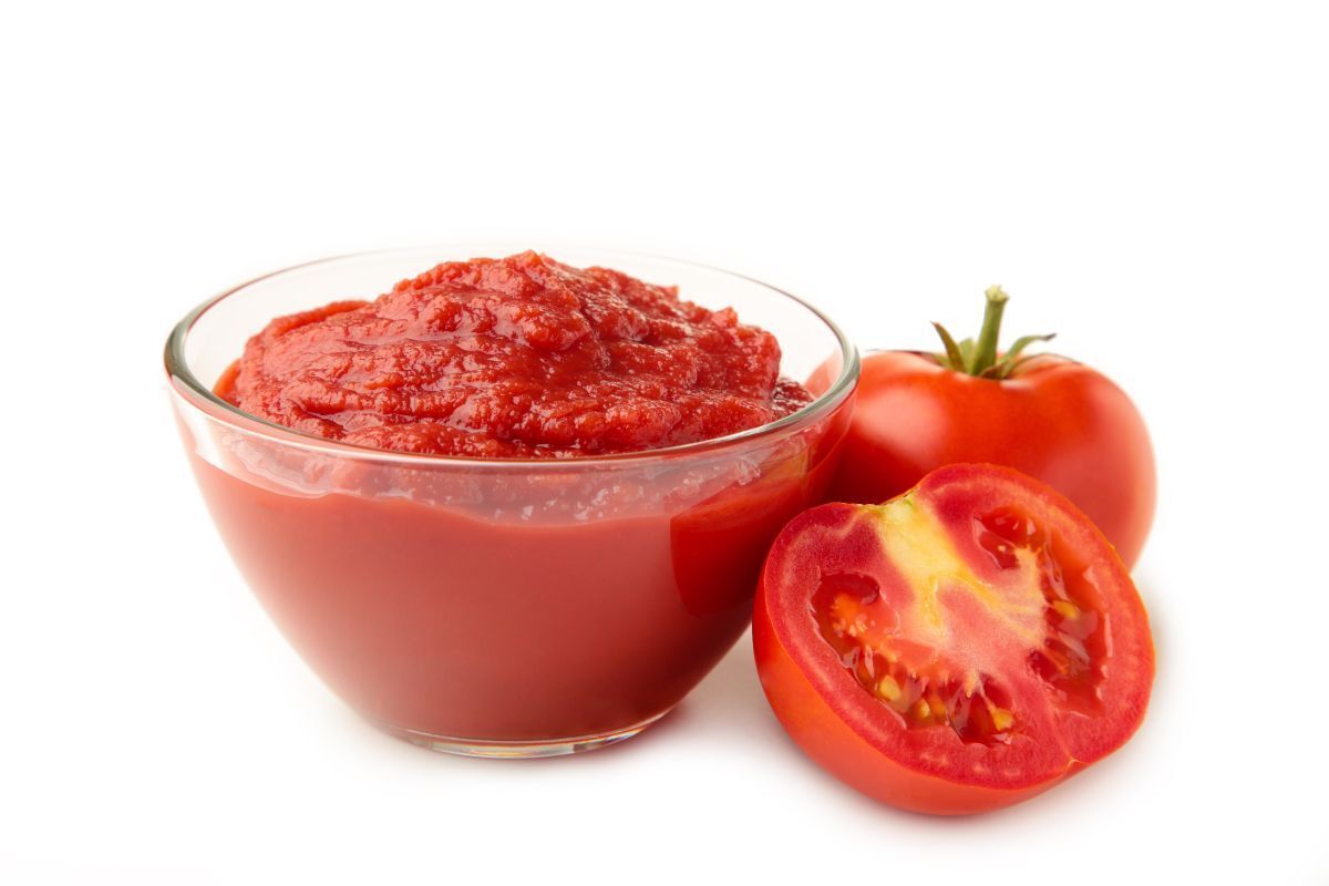 da bị cháy nắng quả cà chua và lát cắt cà chua nằm kế bên chén cà chua xay nhuyễn