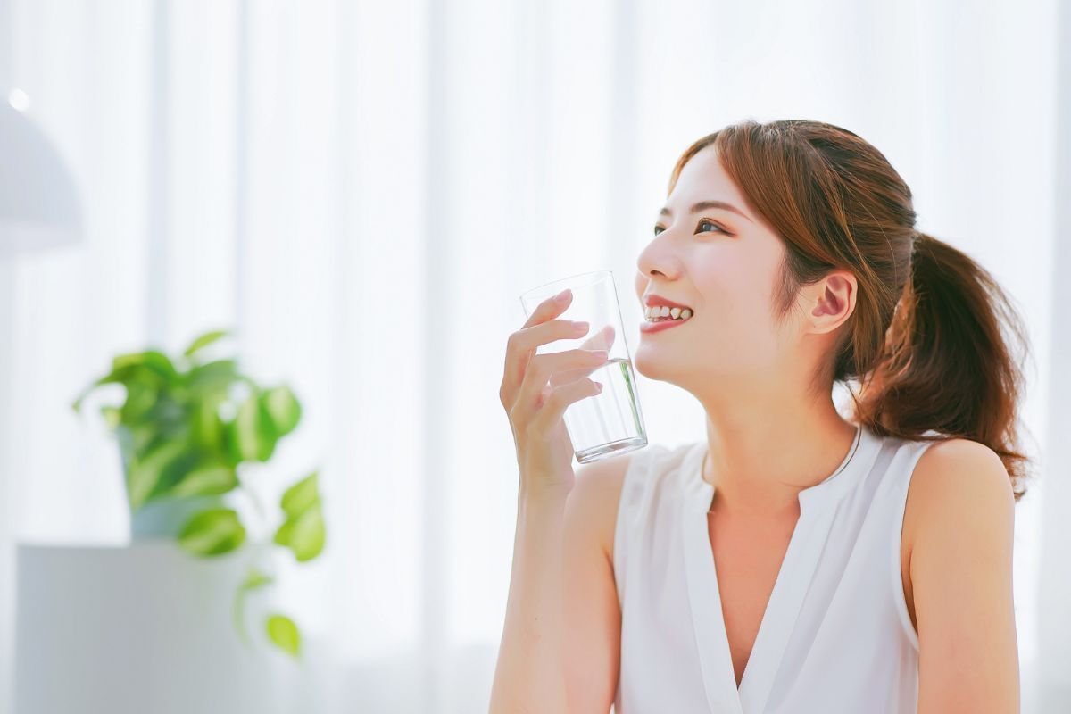 da bị cháy nắng cô gái mỉm cười và cầm cốc đựng nước bằng thuỷ tinh