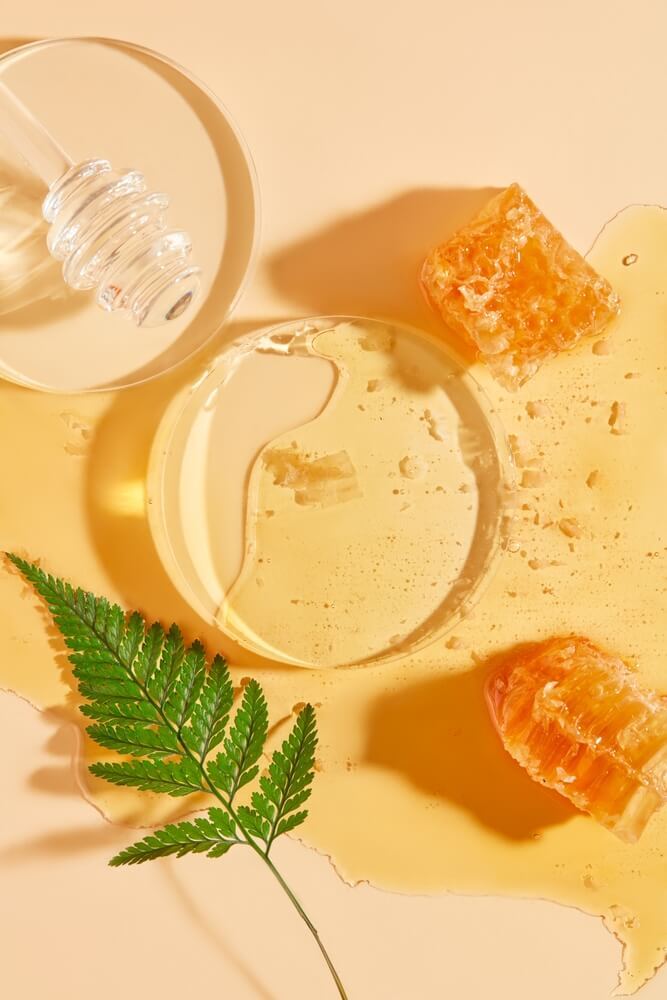 cách tẩy da chết tại nhà bằng mật ong miếng thủy tinh hình tròn được phủ bằng mật ong và sáp ong trên nền vàng