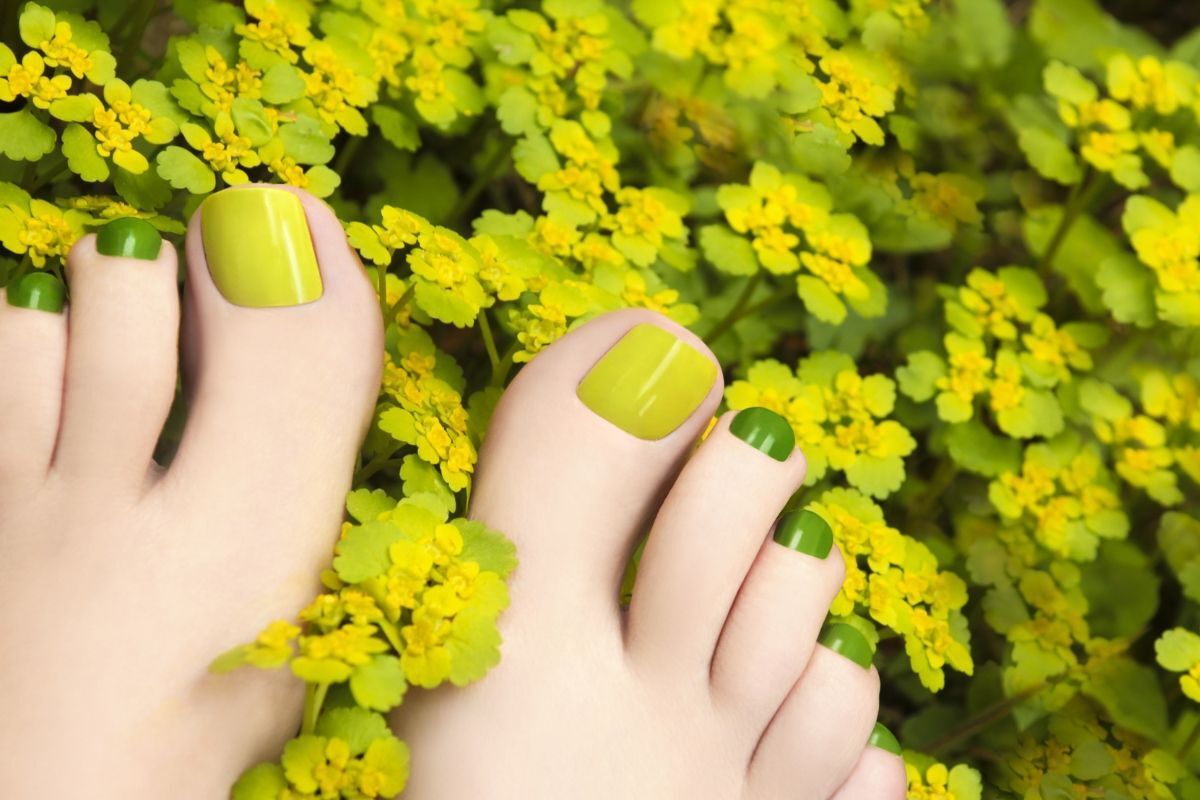 móng chân màu xanh rêu màu sáng bàn chân đặt lên những bông hoa nhỏ màu vàng chanh