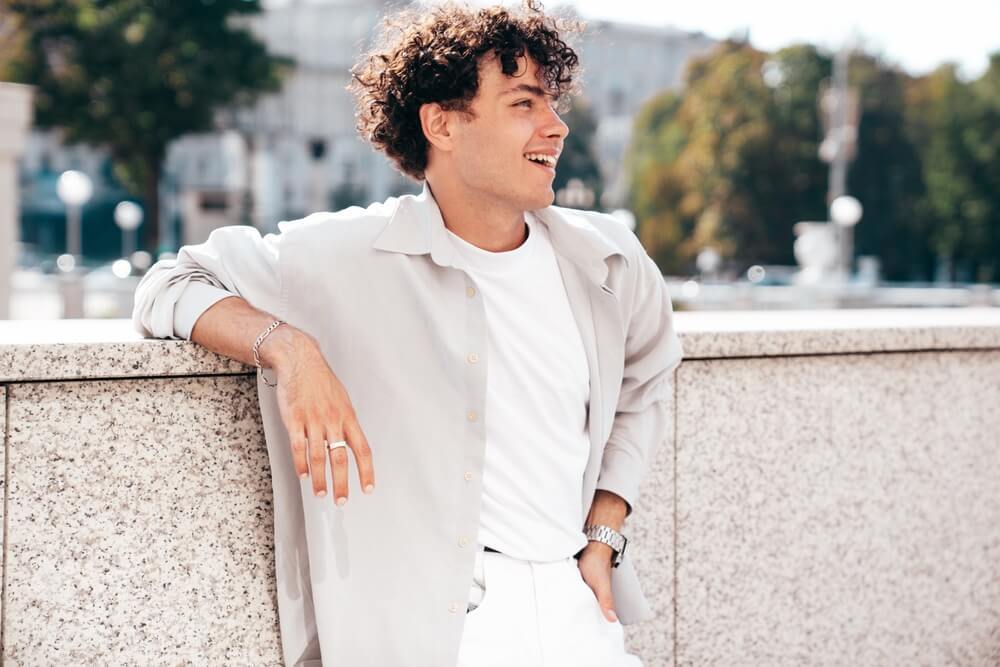 dưỡng tóc nam tóc xoăn chàng trai tóc xoăn đứng dựa lưng vào vách tường ốp đá cười tươi