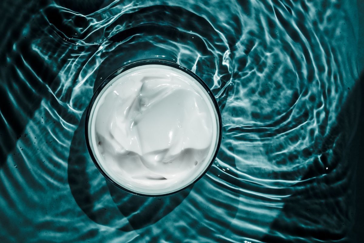 kem dưỡng ẩm cho da dầu mụn góc chụp trực diện từ trên cao xuống chất kem màu trắng nằm trong hủ bao quanh bởi những vệt nước 