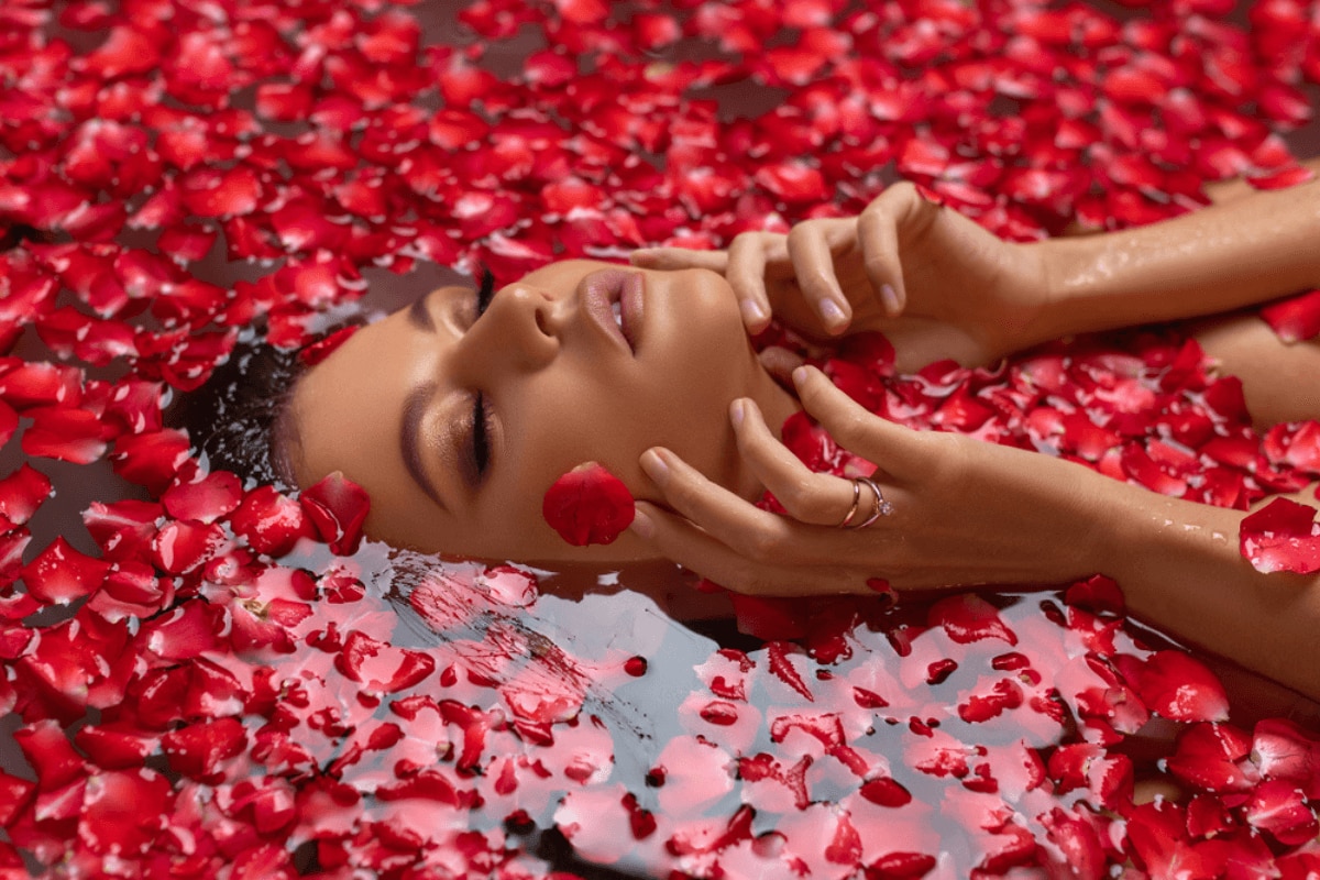 nước hoa hồng có tác dụng gì chân dung người phụ nữ xinh đẹp nhắm mắt ngâm mình trong nước với cánh hoa hồng