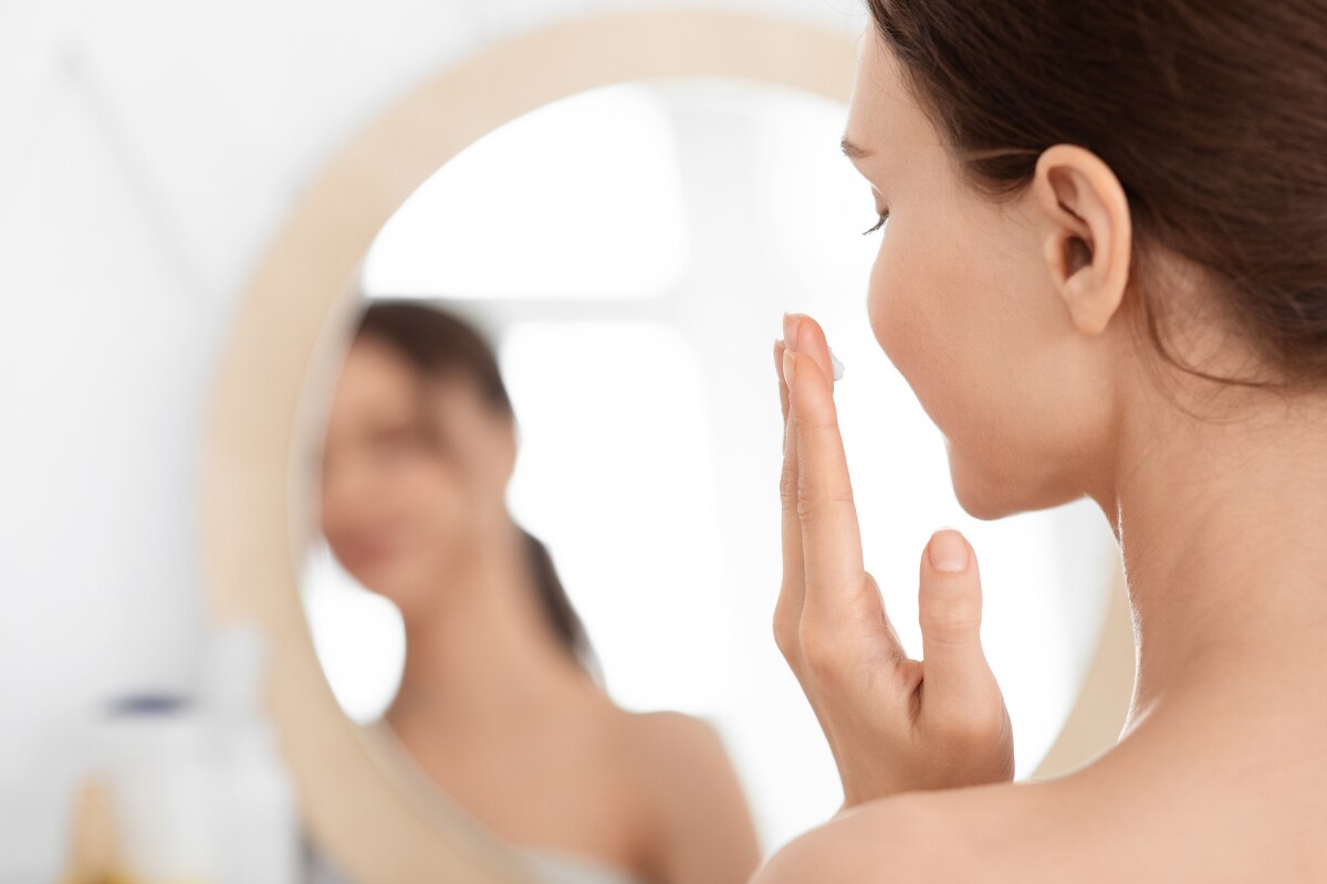 chăm sóc da nhạy cảm bằng kem chống nắng cô gái soi gương thoa kem lên má