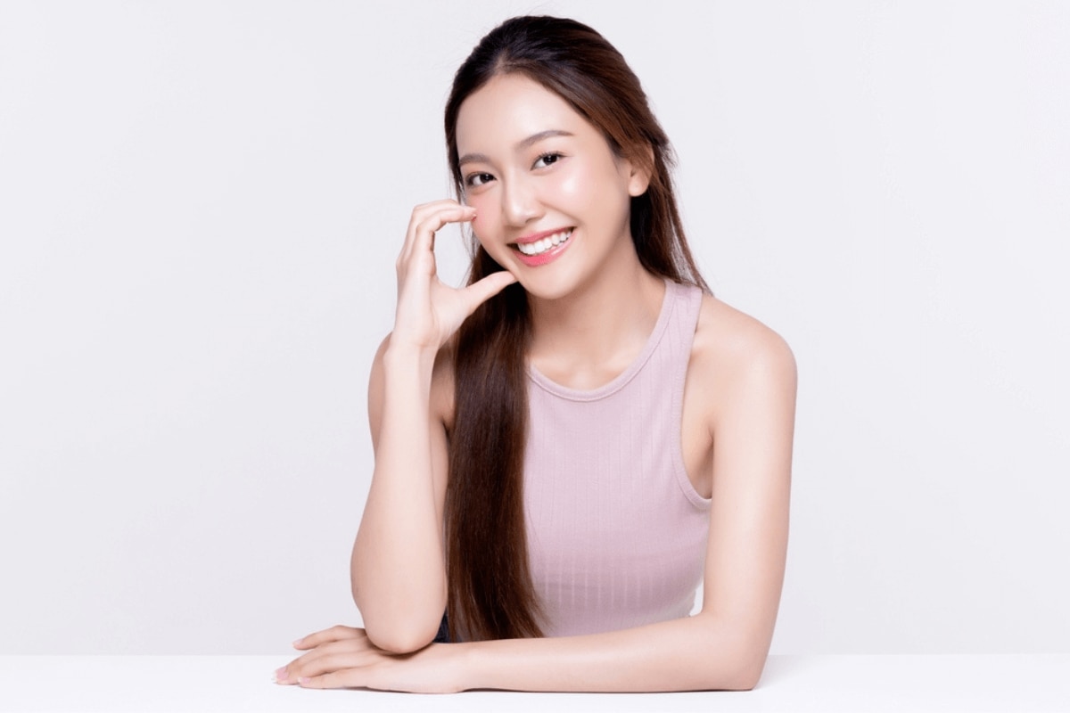 serum là gì serum có tác dụng gì điều trị mụn cô gái ngồi trên bàn lấy tay làm thành hình chữ C cười tươi