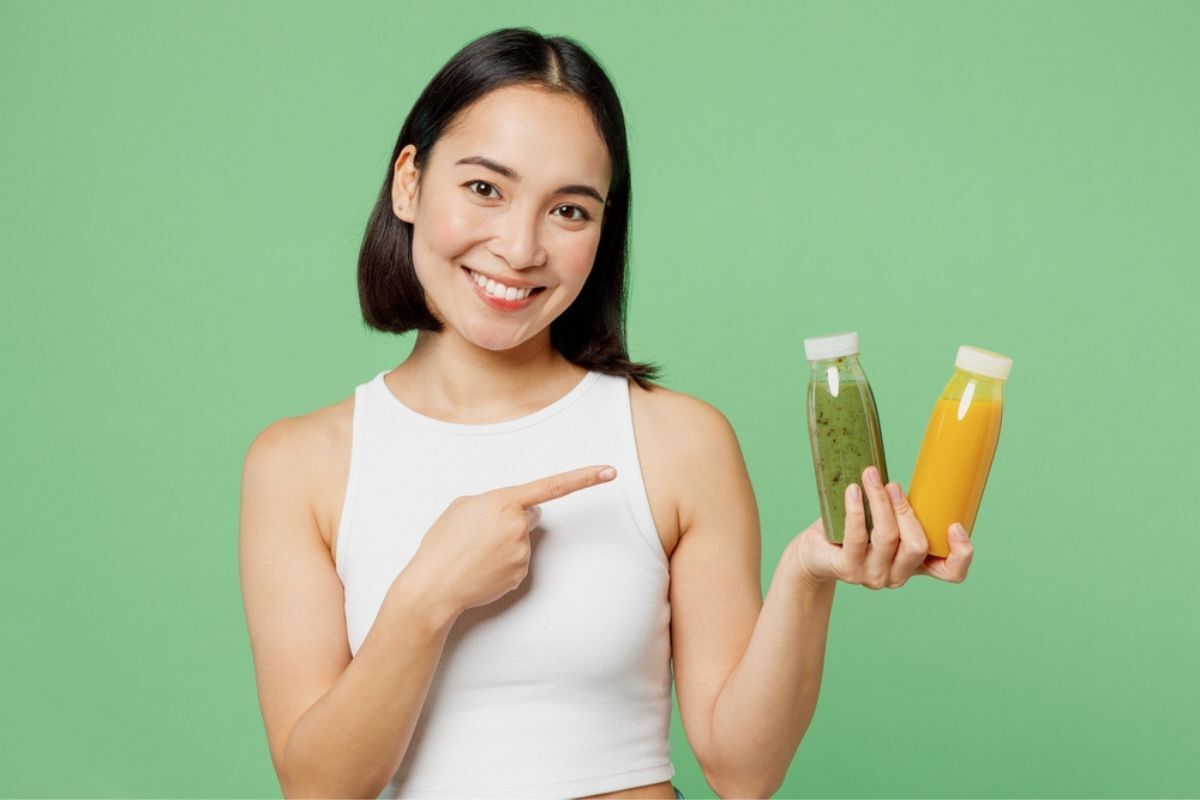 Cách trị tóc bạc sớm ở nữ tóc bạc sớm ở nữ nên uống gì người phụ nữ trẻ mặc quần áo chỉ tay vào chai nước ép trái cây sinh tố rau củ màu vàng và màu xanh lá