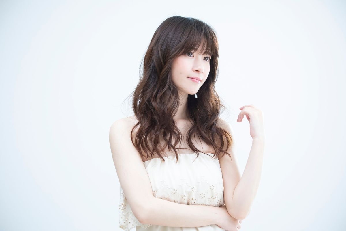 Kiểu tóc đẹp cho mặt tròn cô gái có mái tóc xoăn sóng nước màu nâu đang chống tay 