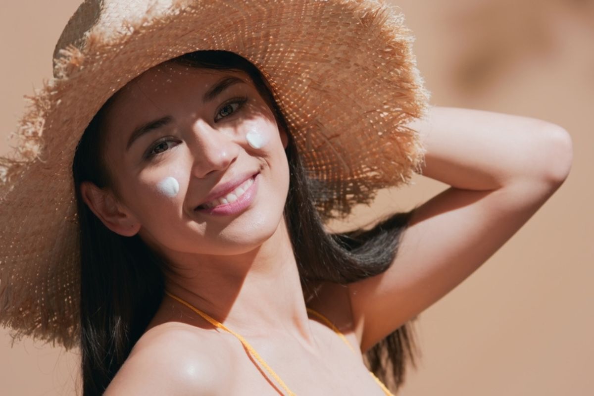 cách bôi lại kem chống nắng cô gái đội nón cối mỉm cười trên mặt có hai vết kem chống nắng ở hai bên má cười tươi dưới ánh nắng