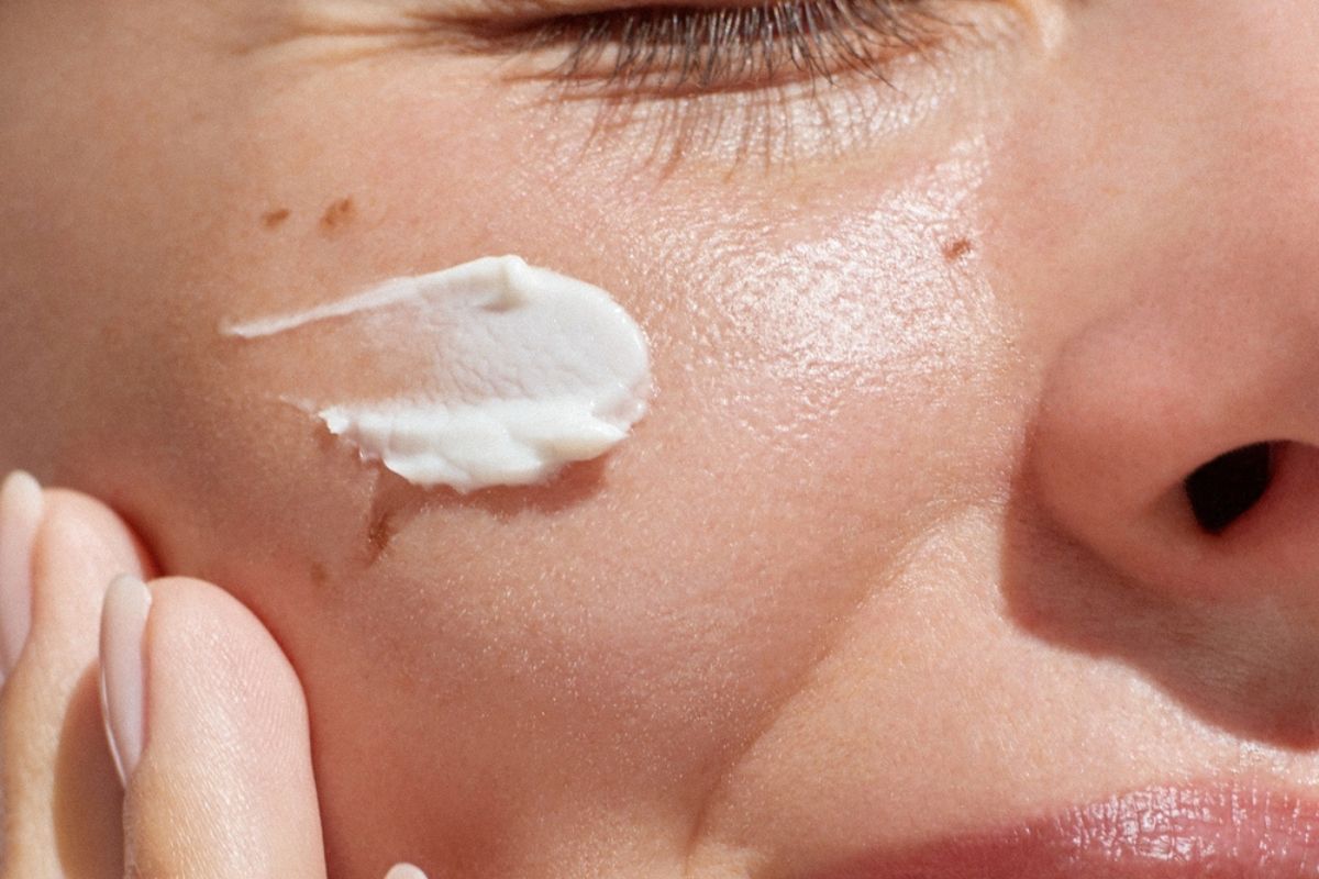 cách bôi lại kem chống nắng chụp cận cô gái thoa kem chống nắng lên má mỉm cười dưới ánh nắng