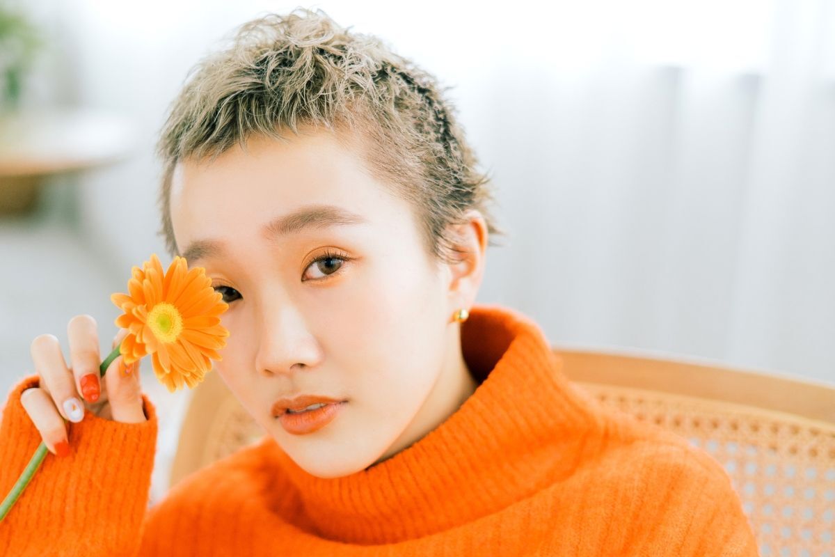 tóc ngắn nữ cá tính tóc pixie tỉa cao cá tính cô gái mặc áo len màu cam tay cầm bông hoa 