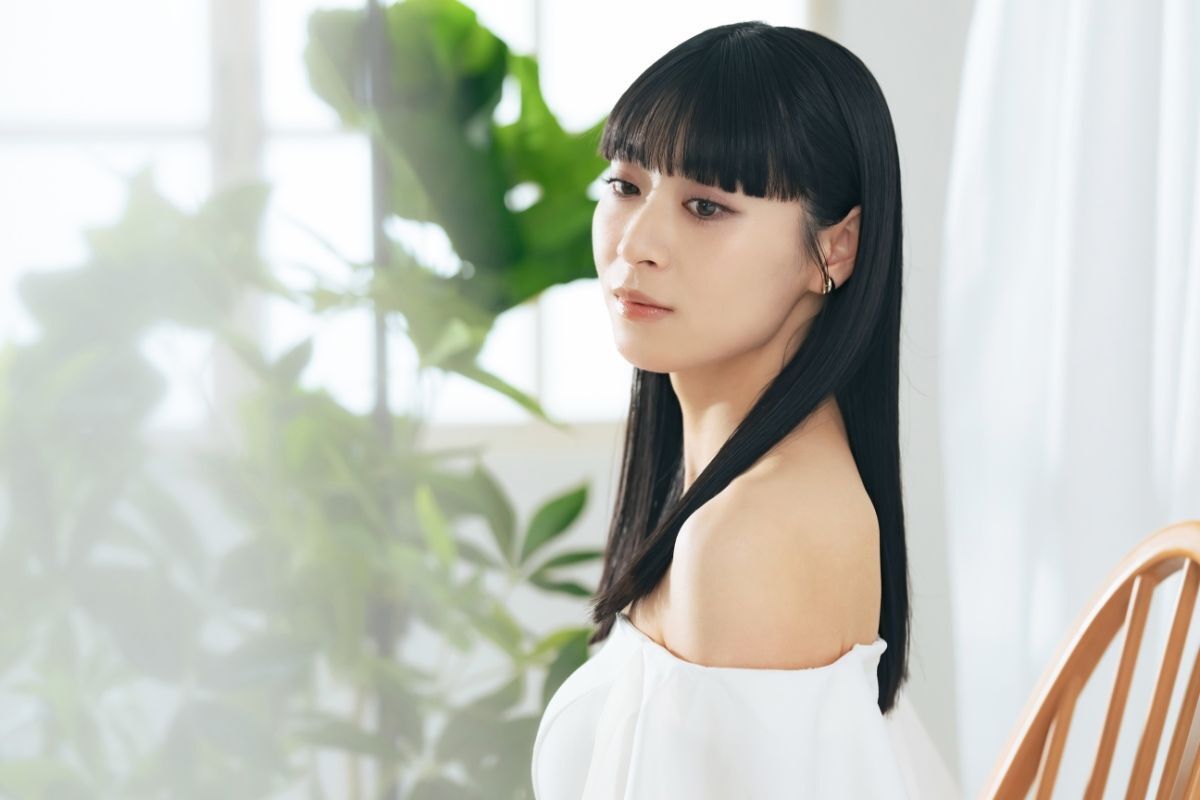 Kiểu tóc cho mặt vuông không bao giờ nên bỏ lỡ cô gái mặc áo trắng trễ vai ngồi trên ghế phía sau có cây xanh