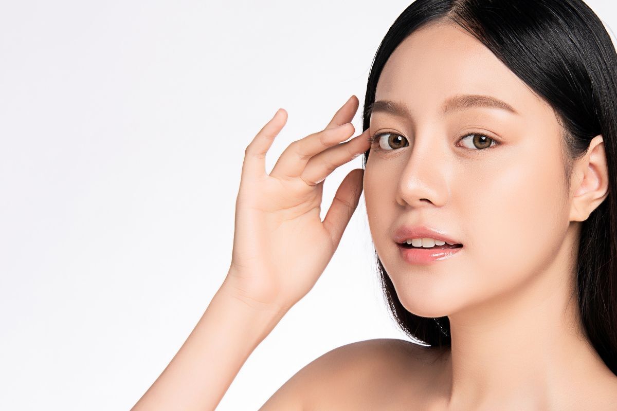 dáng lông mày đẹp cô gái tóc đen đeo kính áp tròng màu nâu lấy tay để hờ lên thái dương trên nền trắng