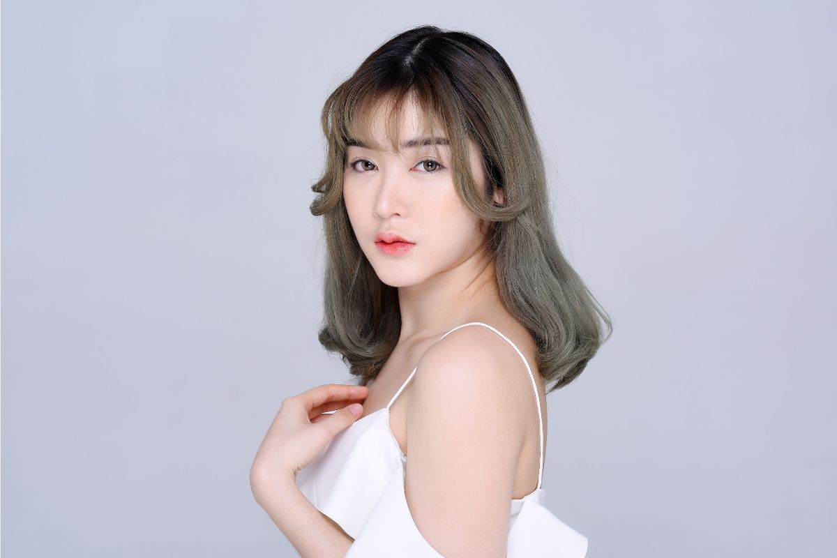 tóc màu nâu tây ánh rêu cô gái tóc uốn cụp ngang vai mặc áo dây màu trắng đứng nhìn nghiêng