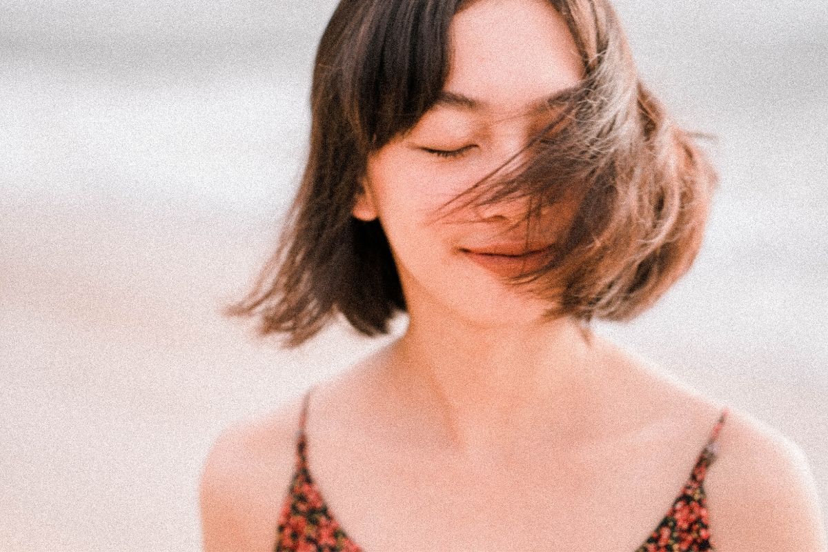 7 kiểu tóc cho mặt vuông nhẹ nhàng mềm mại hơn cô gái mặc váy hai dây hoa màu đỏ đen đang bị gió thổi tung tóc