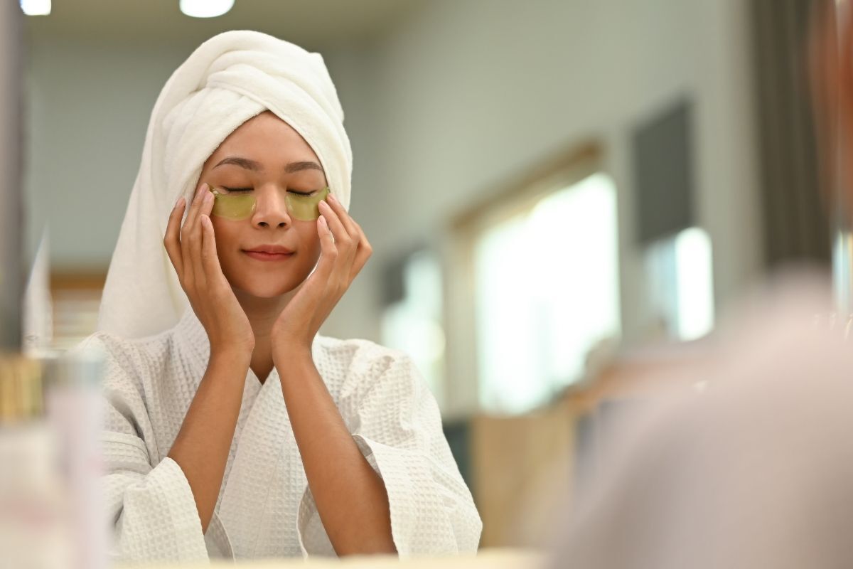 Cách trị thâm mắt cô gái quấn khăn tắm màu trắng trên đầu đang đắp mặt nạ mắt