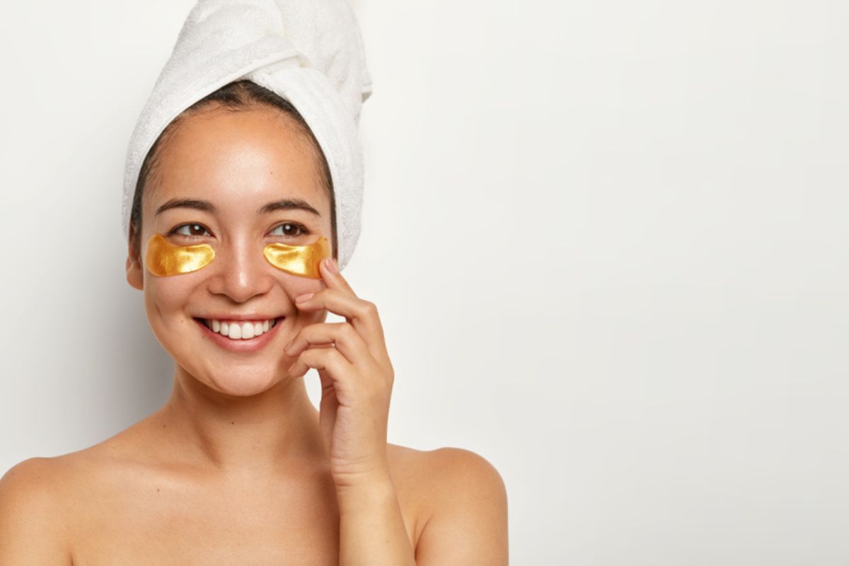 Tinh bột nghệ có tác dụng gì làm mờ quầng thâm mắt người phụ nữ có làn da khỏe mạnh, dán miếng mặt nạ dưới mắt, vui vẻ nhìn sang một bên