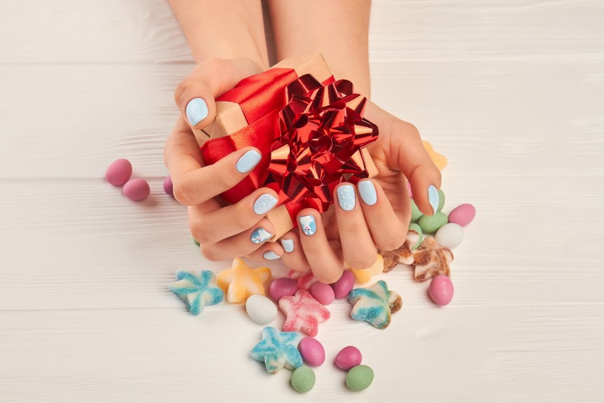 Màu nail Tết cực xinh bàn tay sơn móng màu xanh dương và cầm hộp quà thắt nơ màu đỏ