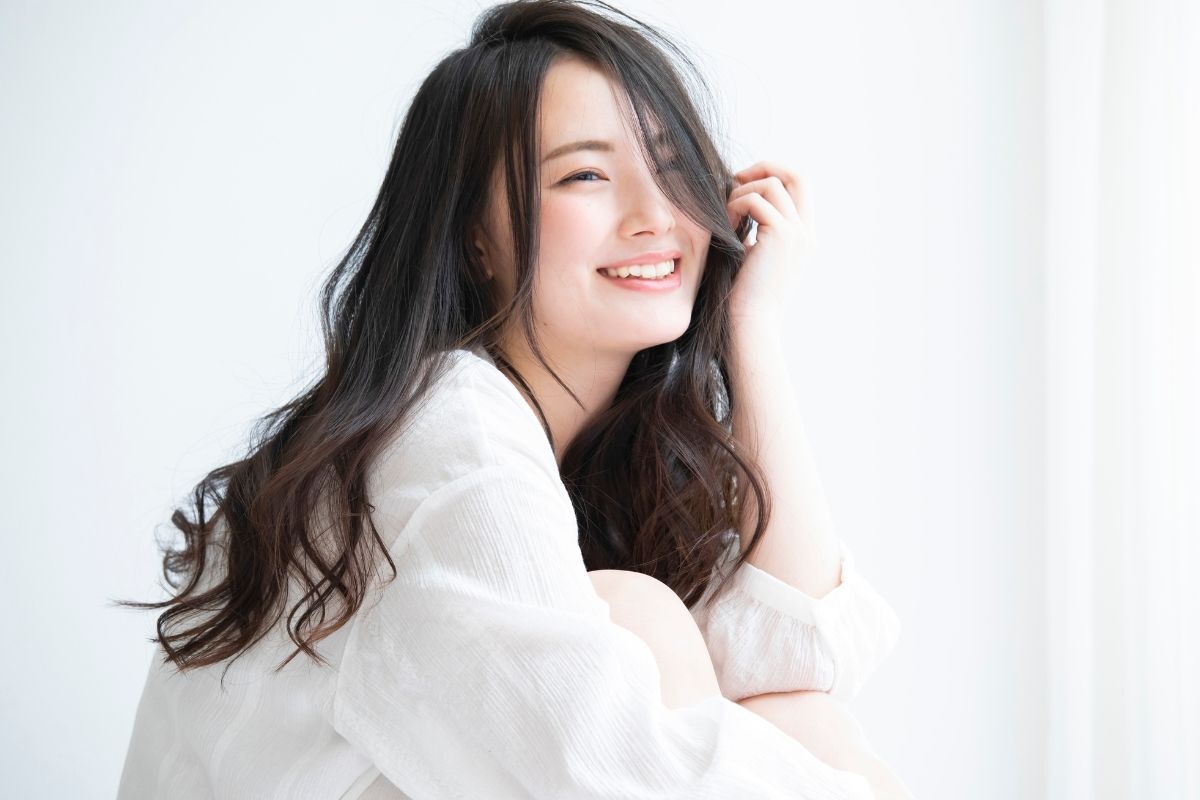 Tóc layer nữ ngang lưng cô gái đang cười tươi một tay chạm tóc