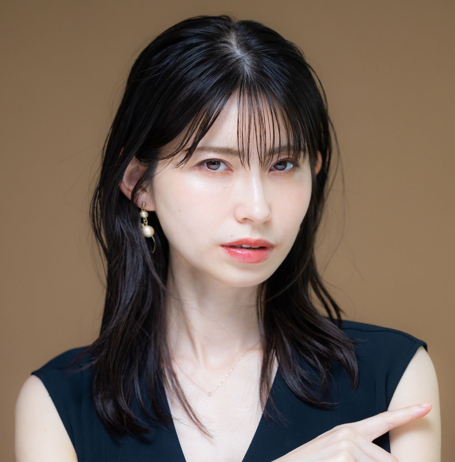 Tóc layer nữ mái thưa cô gái chạm một tay vào cằm trên phông nền màu nâu be