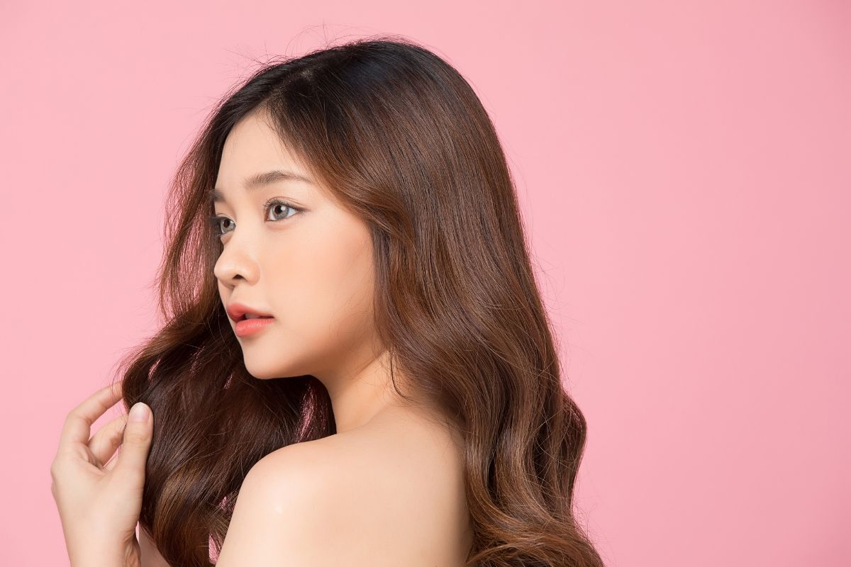 Tóc xoăn sóng nước cho mặt dài cô gái tóc xoăn đang nhìn nghiêng về phía bên phải trên phông nền màu hồng