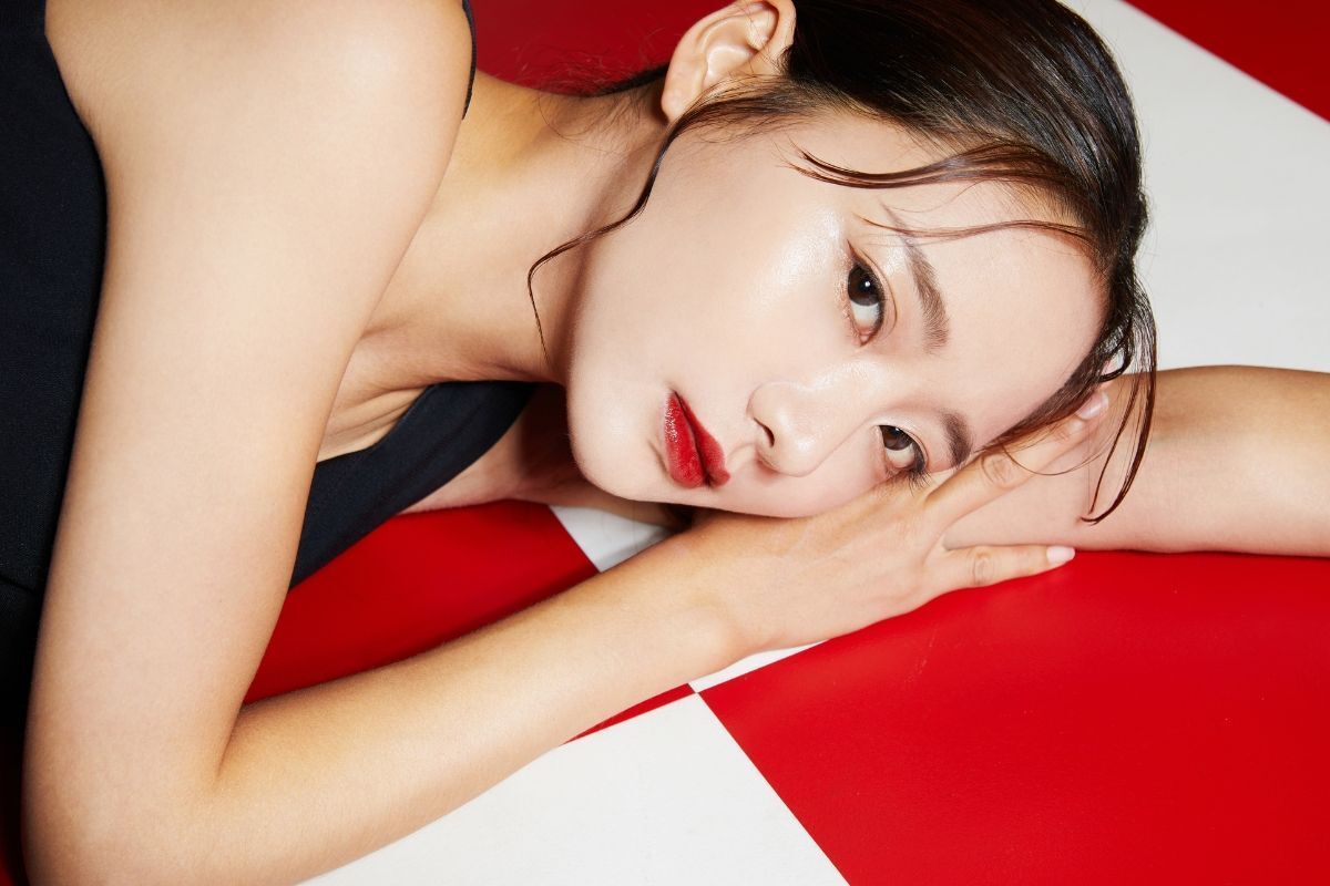 Cách lựa chọn màu son phù hợp với tone da cô gái nằm gối đầu lên tay tô son đỏ mặc váy đen nền đỏ và trắng