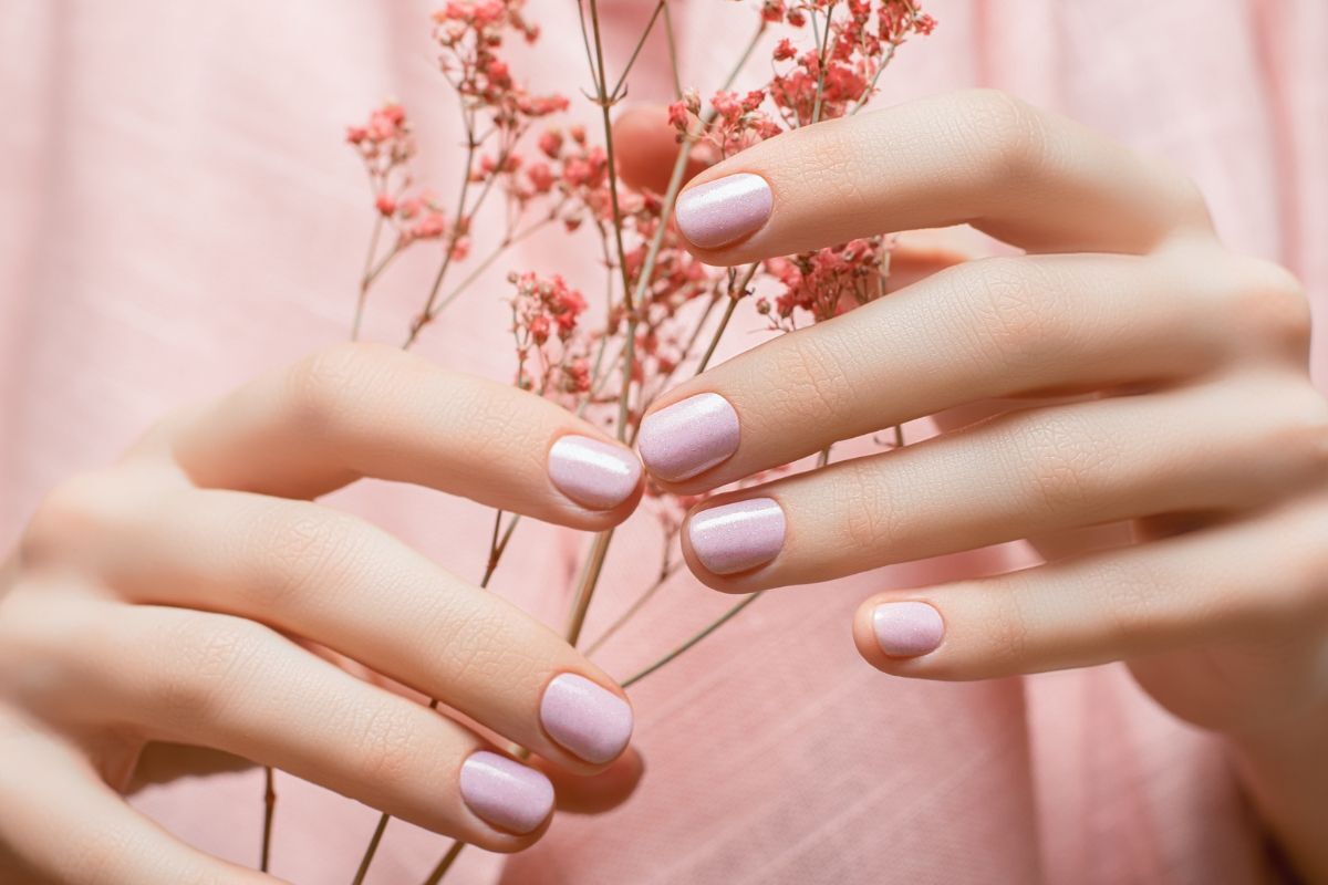 móng tay màu hồng bàn tay cầm nhành hoa trên nền vải hồng 