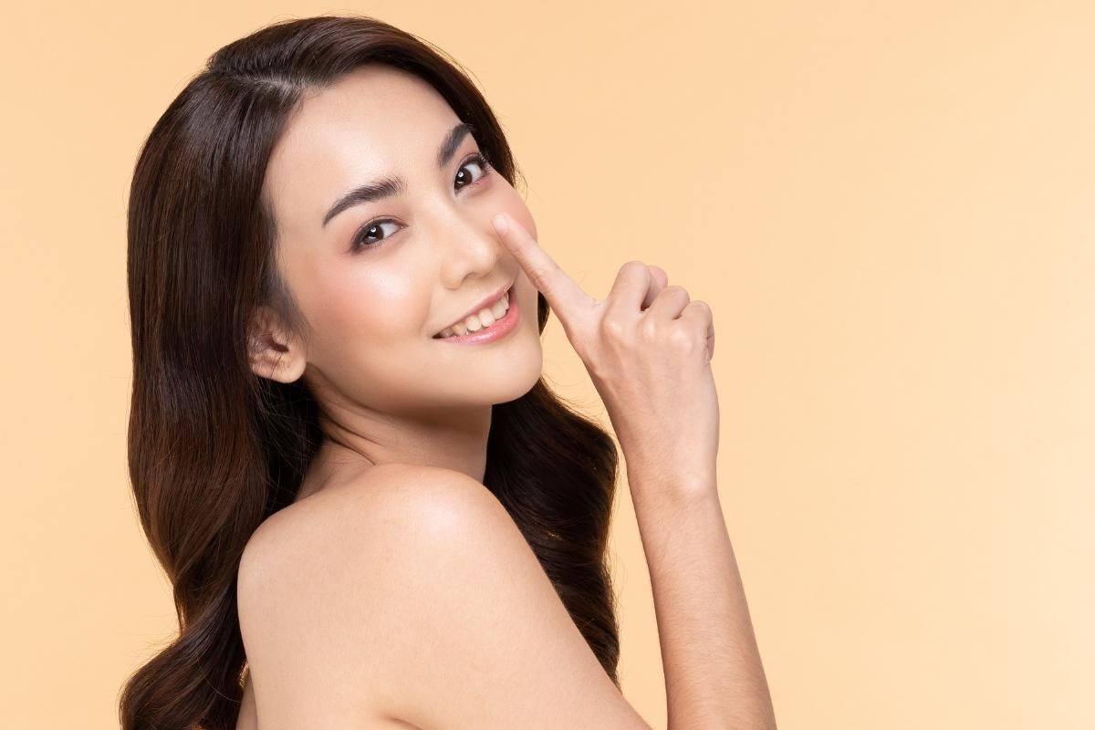 Cách làm mũi nhỏ lại cô gai cô ái chỉ ngón tay trỏ vào mũi trên nền vàng
