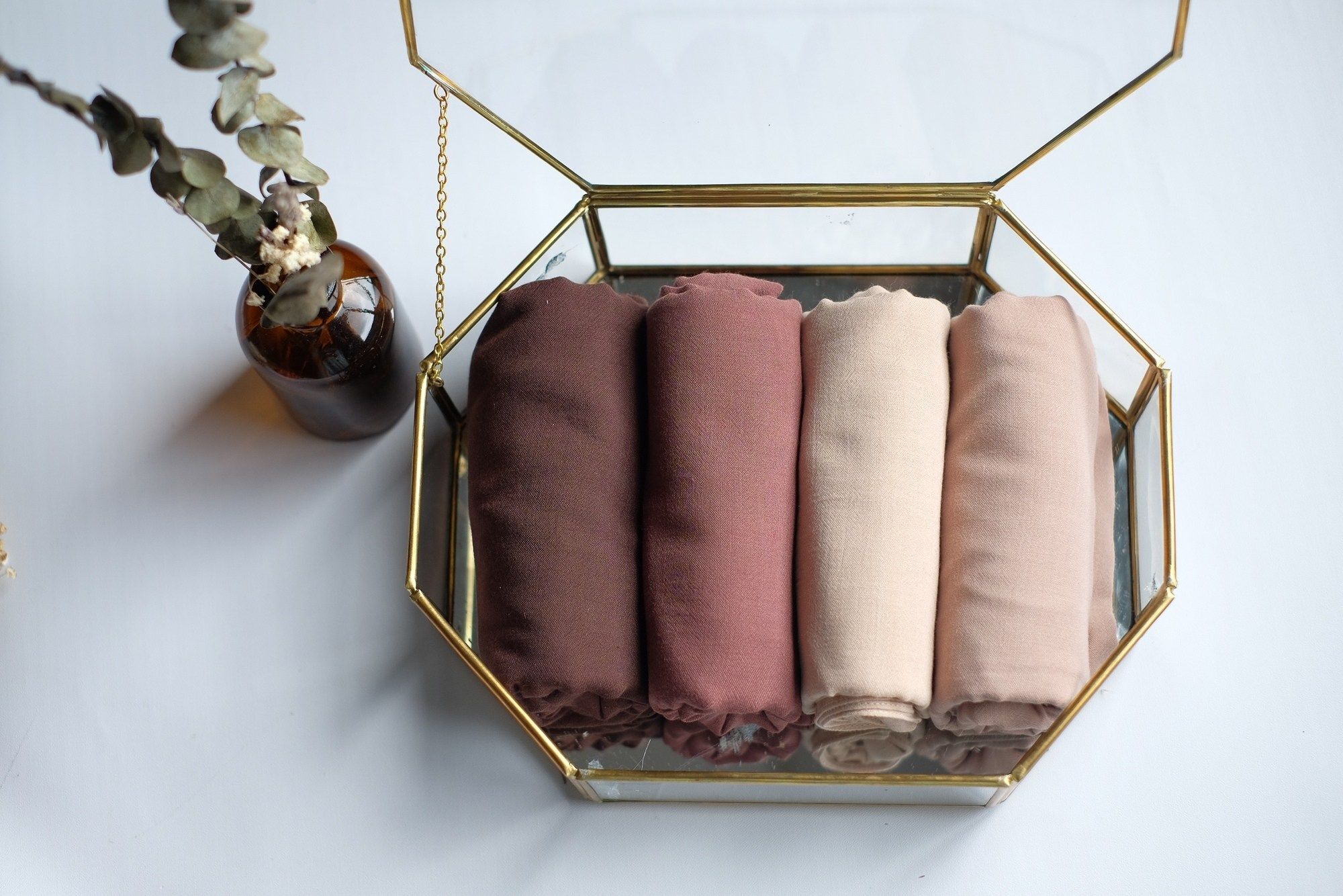 Empat hijab segi empat dilipat rapi dalam box kaca.