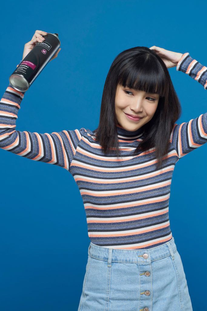 Wanita asia dengan rambut pendek dan poni menyemprotkan hairspray pada seluruh rambutnya